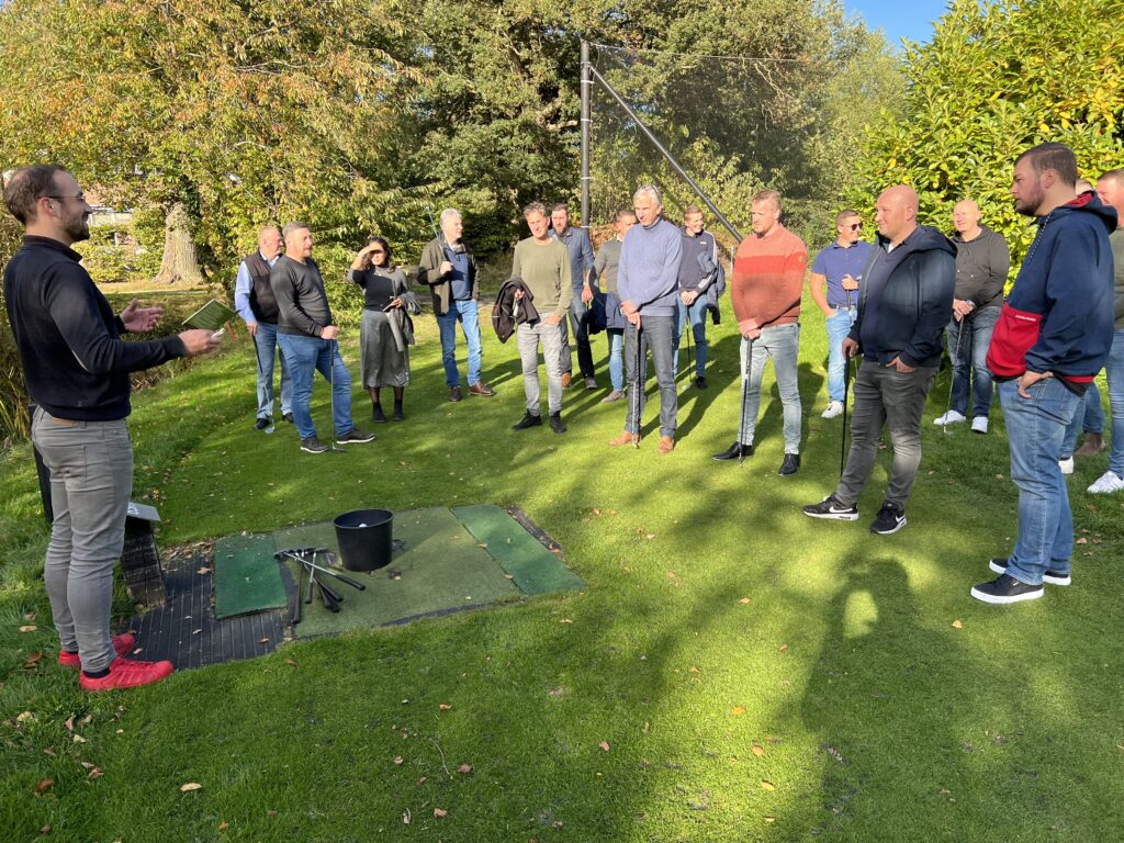 Partnermiddag van Jordahl Gevelverankering. 17 mensen staan om het grasveld en krijgen uitleg van een man voor midgetgolfen.