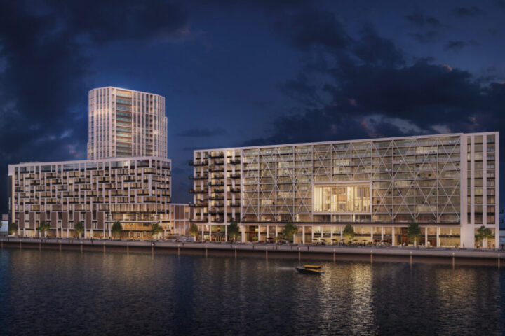 Een heel groot bedrijfspand naast het water. Het is donker buiten en er schijnen overal lichtjes vanuit de kamers van het gebouw.